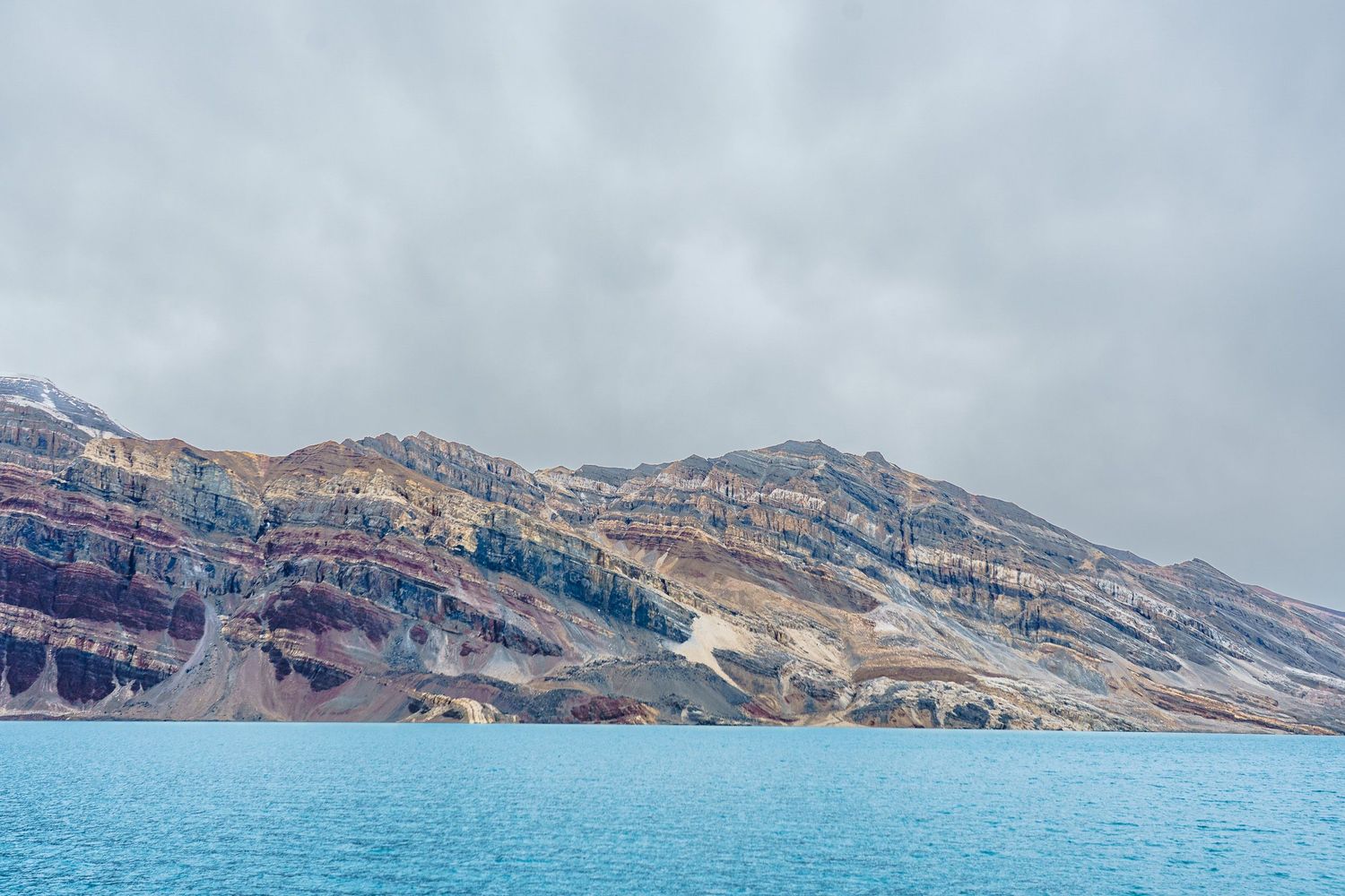 Stunning panoramic view of cliffs and calm blue waters of Death Valley Lake with rugged mountain peaks in the background.
