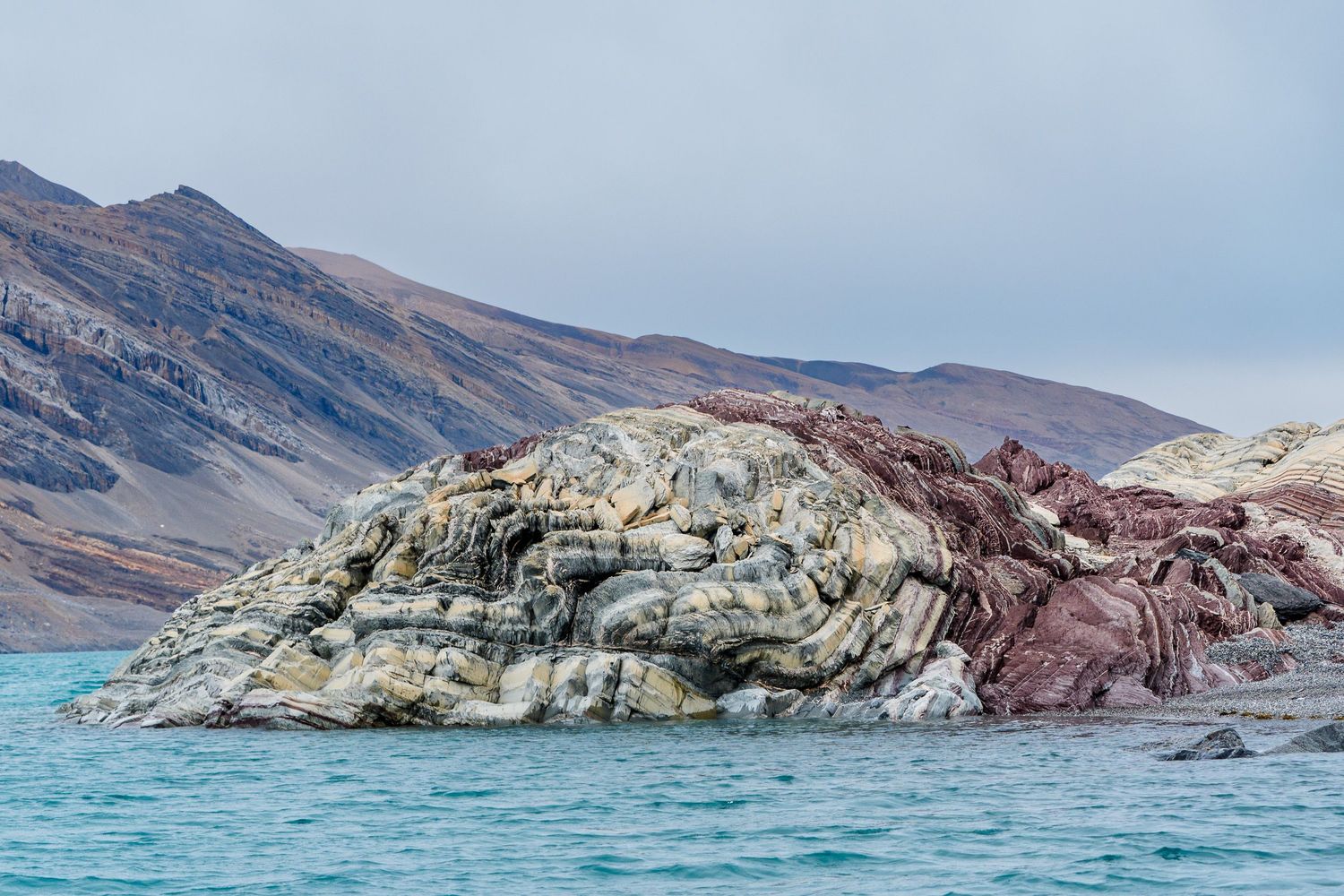 Striped rock formations and rugged cliffs along a turquoise coastline show dramatic geological layers and patterns.