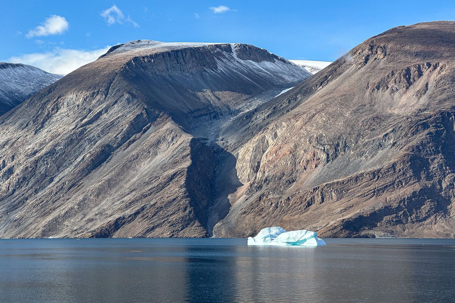 A dramatic panoramic view of rugged mountain ranges and fjords with icebergs floating in pristine blue waters in Greenland.