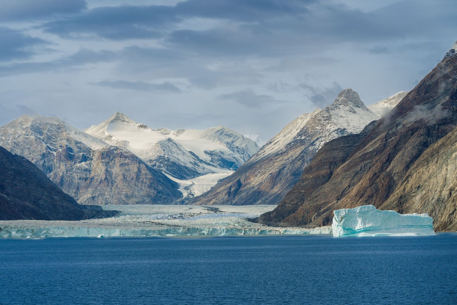 Snow-capped mountains tower over a blue glacial fjord with floating icebergs in Alaska's pristine wilderness.