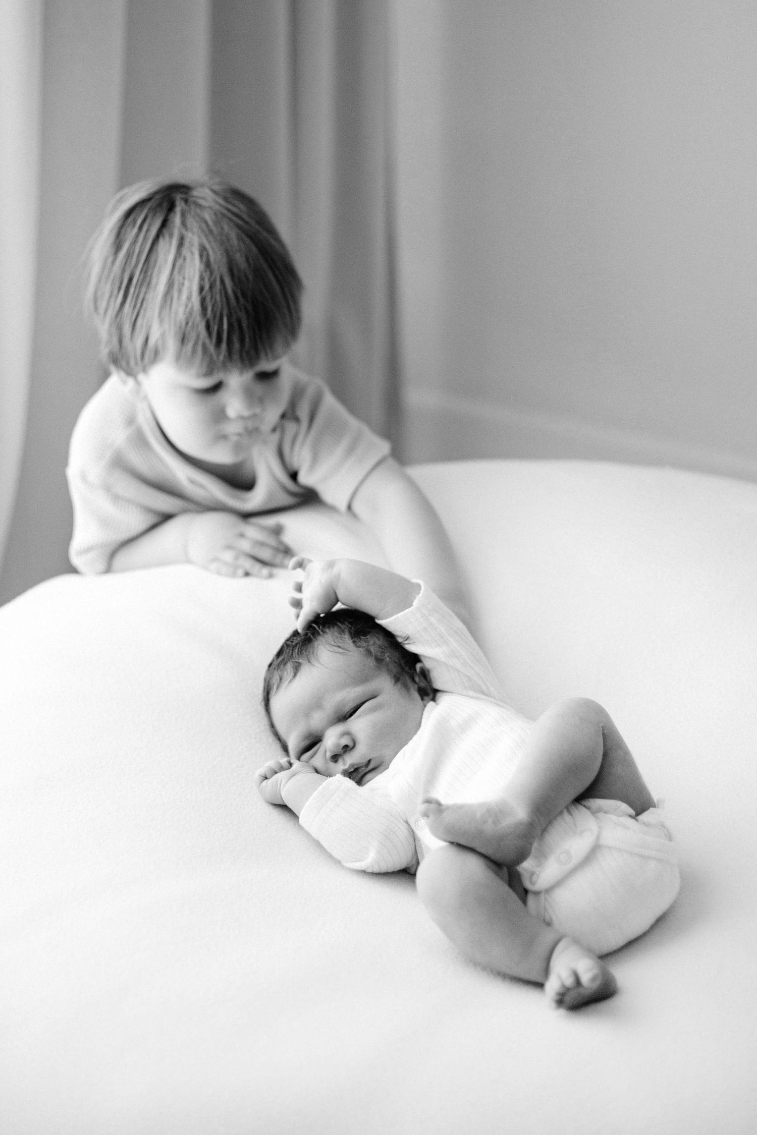 Black and white sequence of photos showing a sleepy baby lying on white bedding in different relaxed positions.