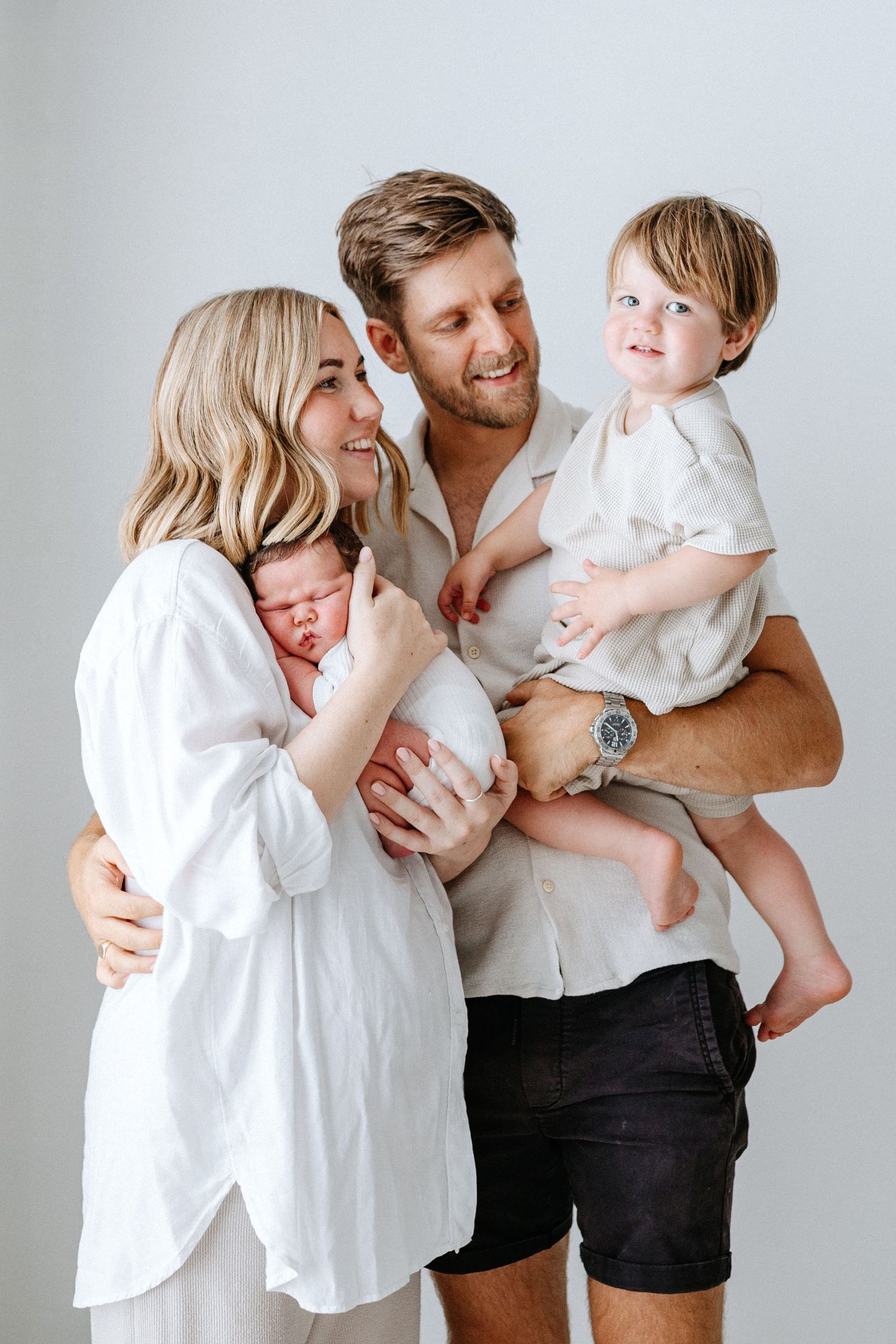 A family wearing black and white clothing shares playful tender moments in a series of four studio portraits.