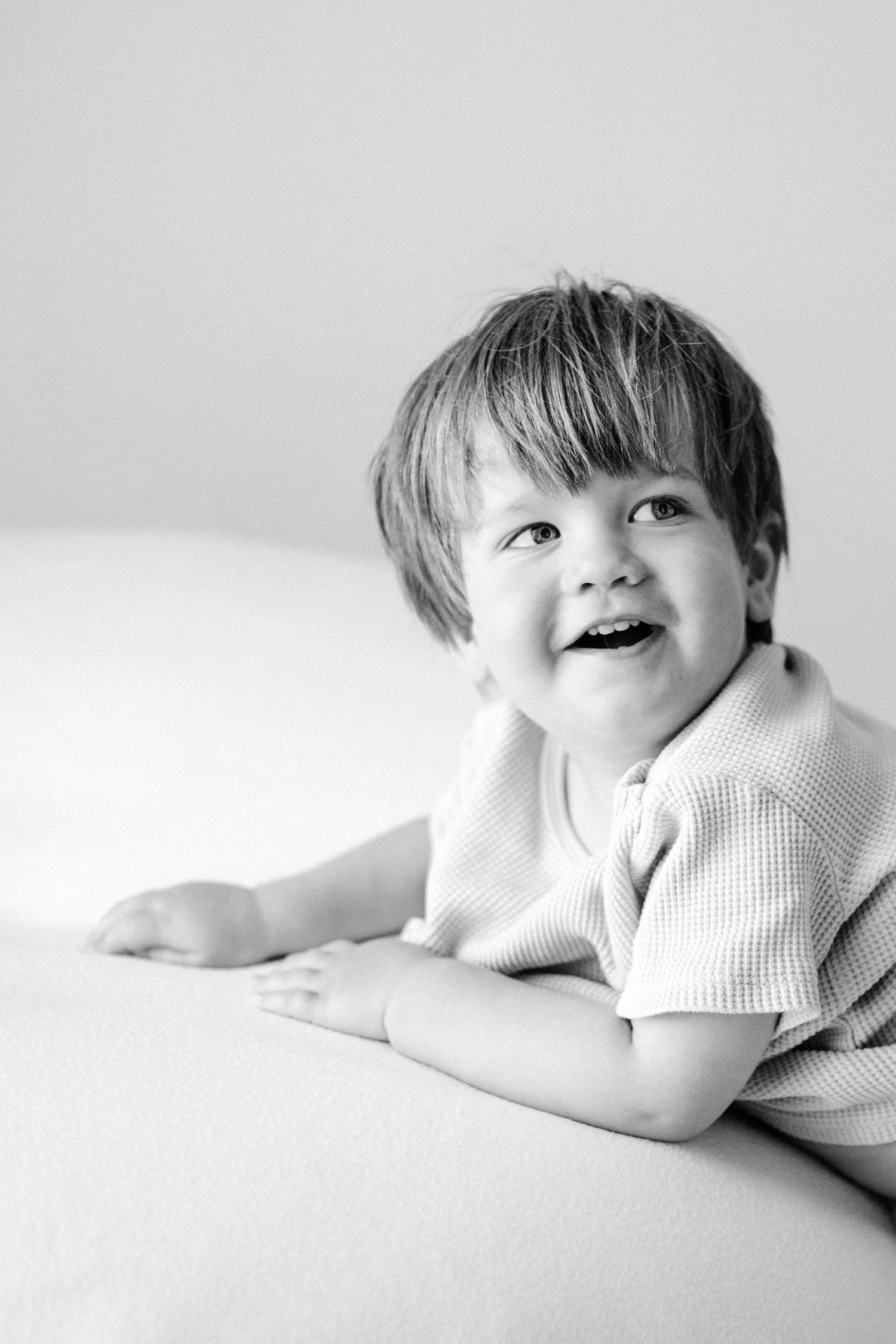 Black and white photograph series showing a small child lying on a white surface in a playful and relaxed mood.