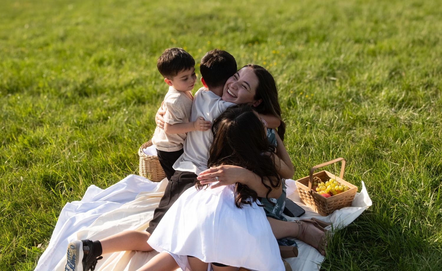 Couple shares romantic moments on grassy lawn in sunset light wearing white outfits during outdoor photoshoot.