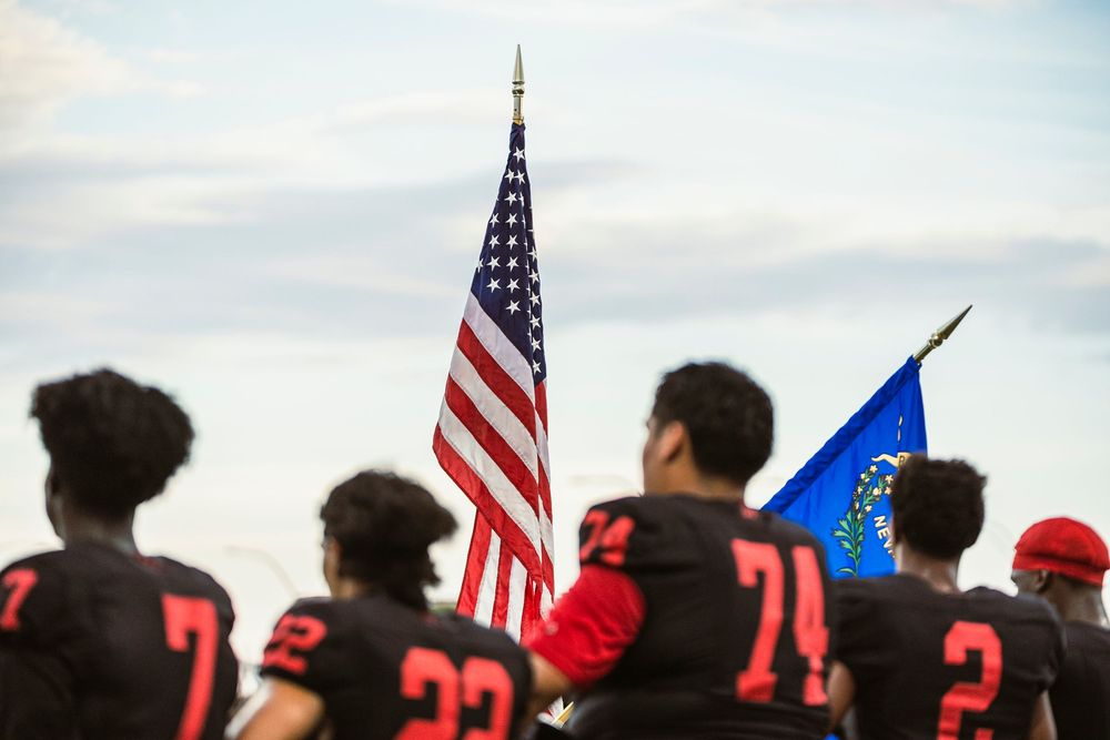 Football players standing, looking at the American Flag before the National Anthem