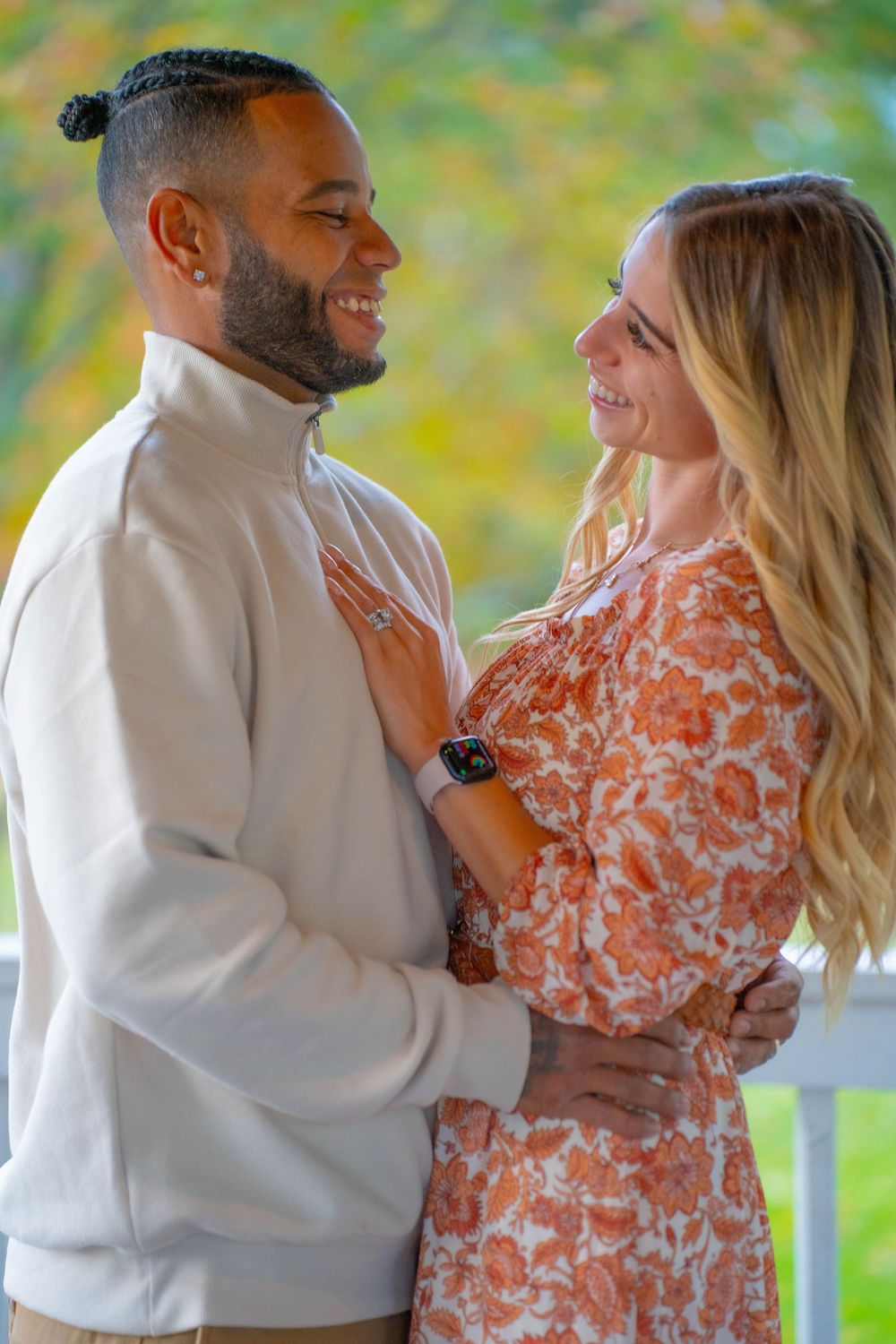 Couple in floral dress and white sweater embracing outdoors during autumn photoshoot.