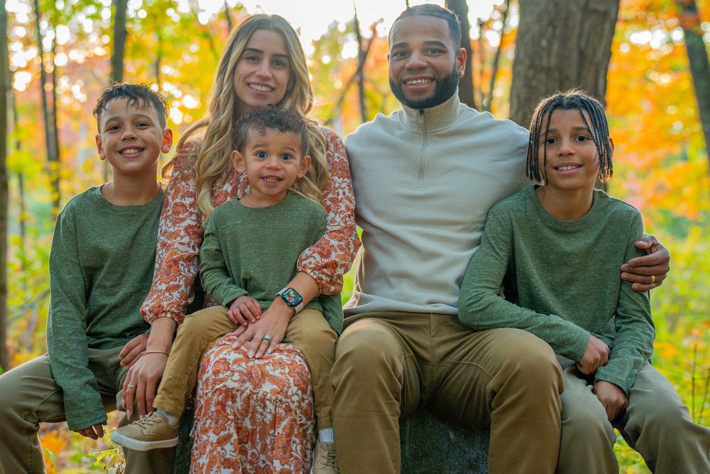Family sitting together on grass during fall season photoshoot.