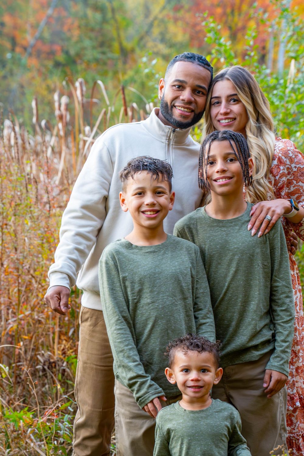 Family portrait with coordinated green outfits against autumn foliage background.