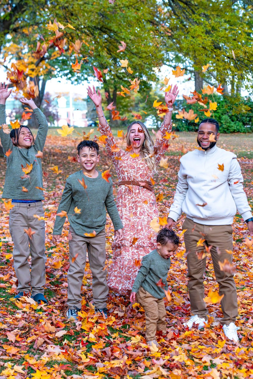 Family playing in pile of colorful autumn leaves during outdoor photoshoot.