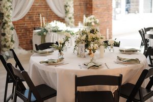 Round dining tables with white linens and floral centerpieces set up in an elegant brick-walled reception venue.