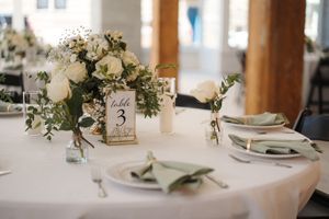 Elegant wedding table setting with white floral centerpiece, white linens, and rustic table number display.