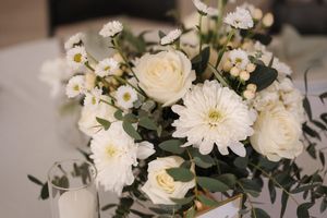 A romantic white floral centerpiece arrangement featuring roses, daisies and delicate small blooms with greenery.