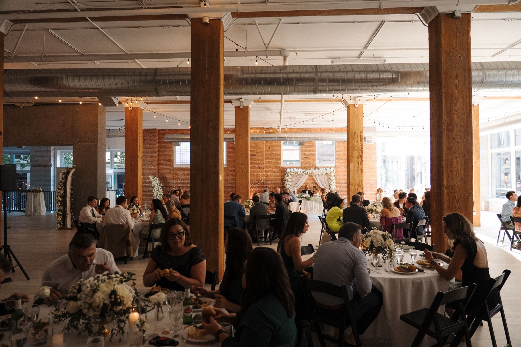 A series of candlelit banquet tables arranged in a reception venue with guests seated for a wedding celebration.
