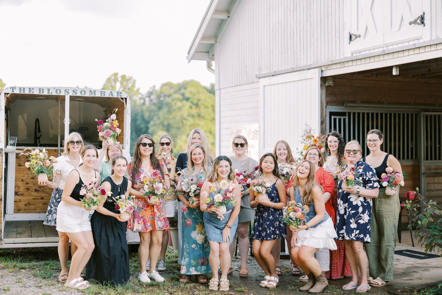 Wedding party in colorful dresses and formal attire pose together for celebratory group photos outside a white building.