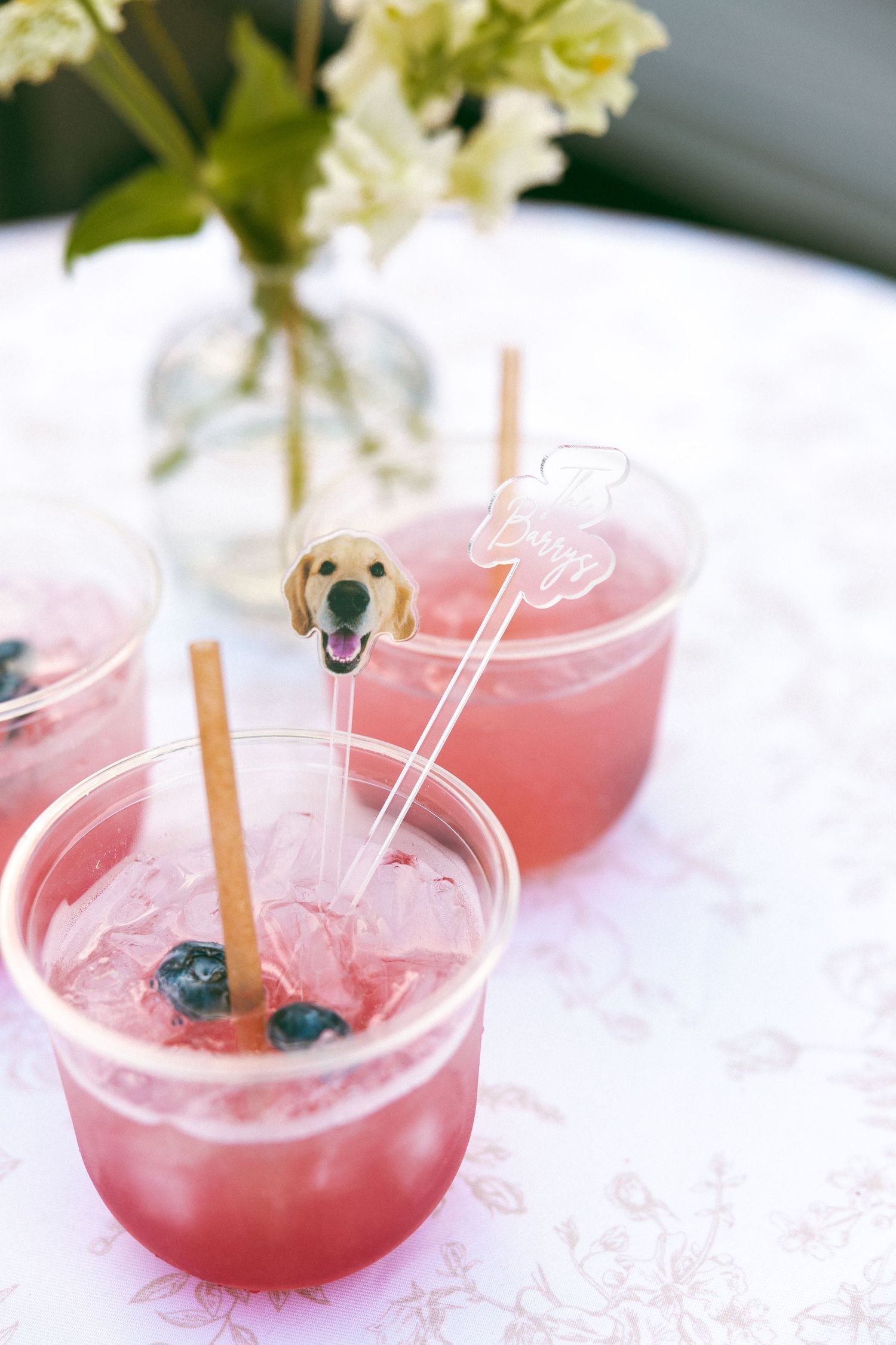 Pink signature cocktails garnished with blueberries and flowers served on white linens.