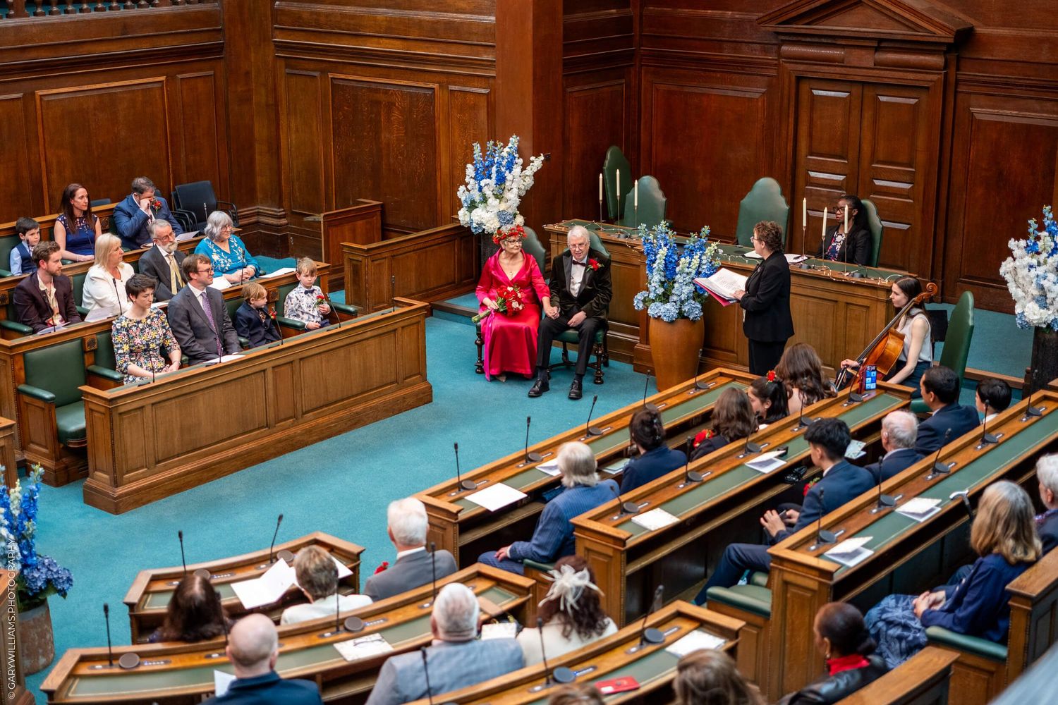 Elevated view of a parliamentary chamber session with wooden benches and people seated in formal attire.