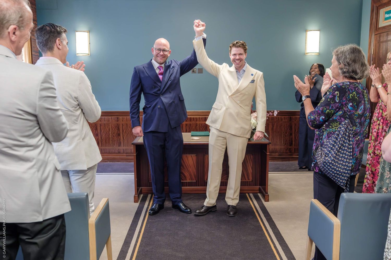 Two individuals celebrating with raised hands during a ceremony while attendees applaud in a chapel setting.