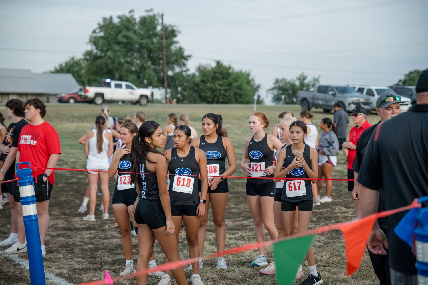 Large group of runners awaiting the start of a trail race on a muddy course in overcast weather.