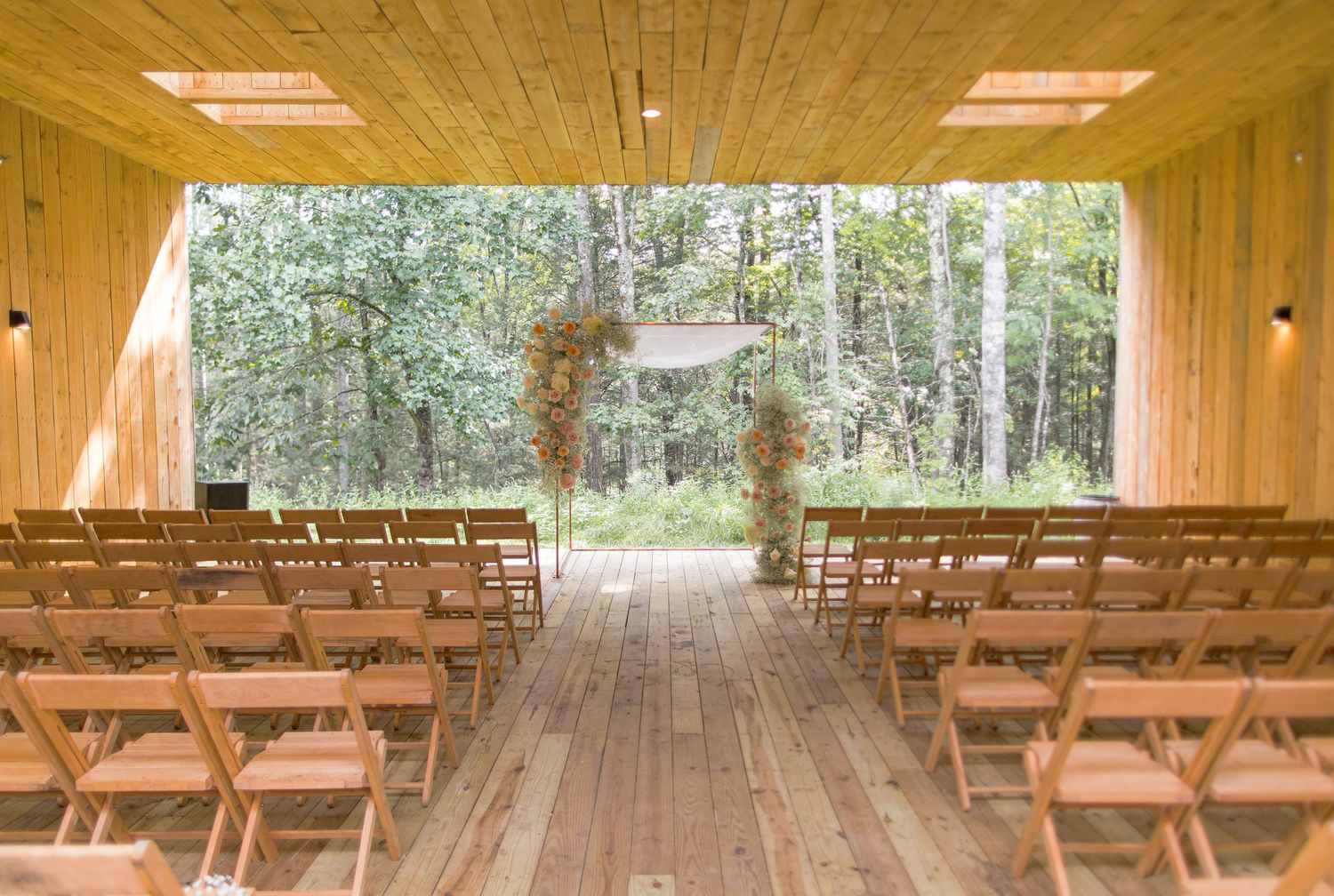 Wooden benches arranged in rows inside a rustic chapel with natural light streaming through glass windows and wood paneling.