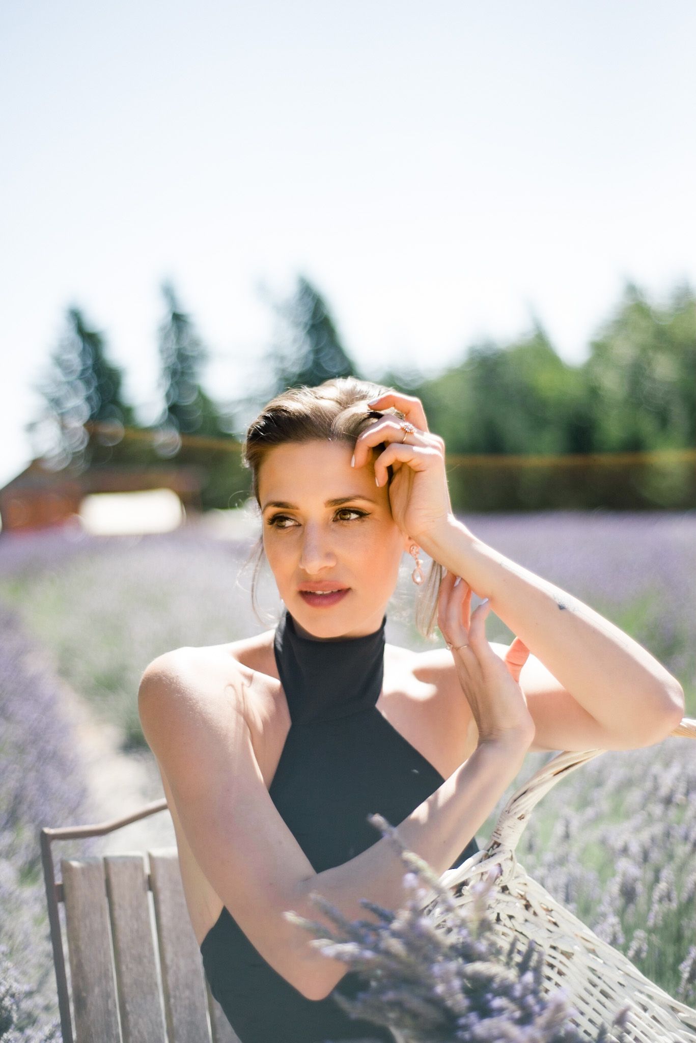 A person in a black sleeveless top poses elegantly in a blooming lavender field on a sunny summer day.