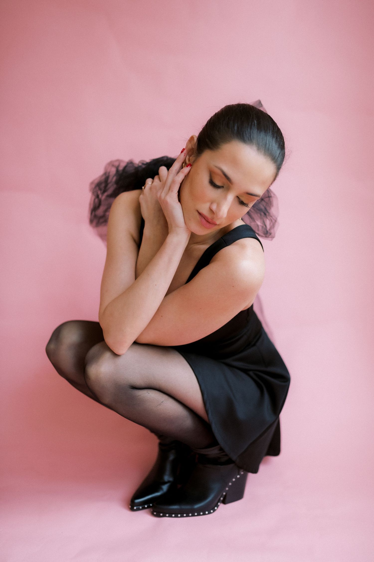 A figure in a black dress strikes elegant artistic poses against a pink studio backdrop, creating a minimalist boudoir series.