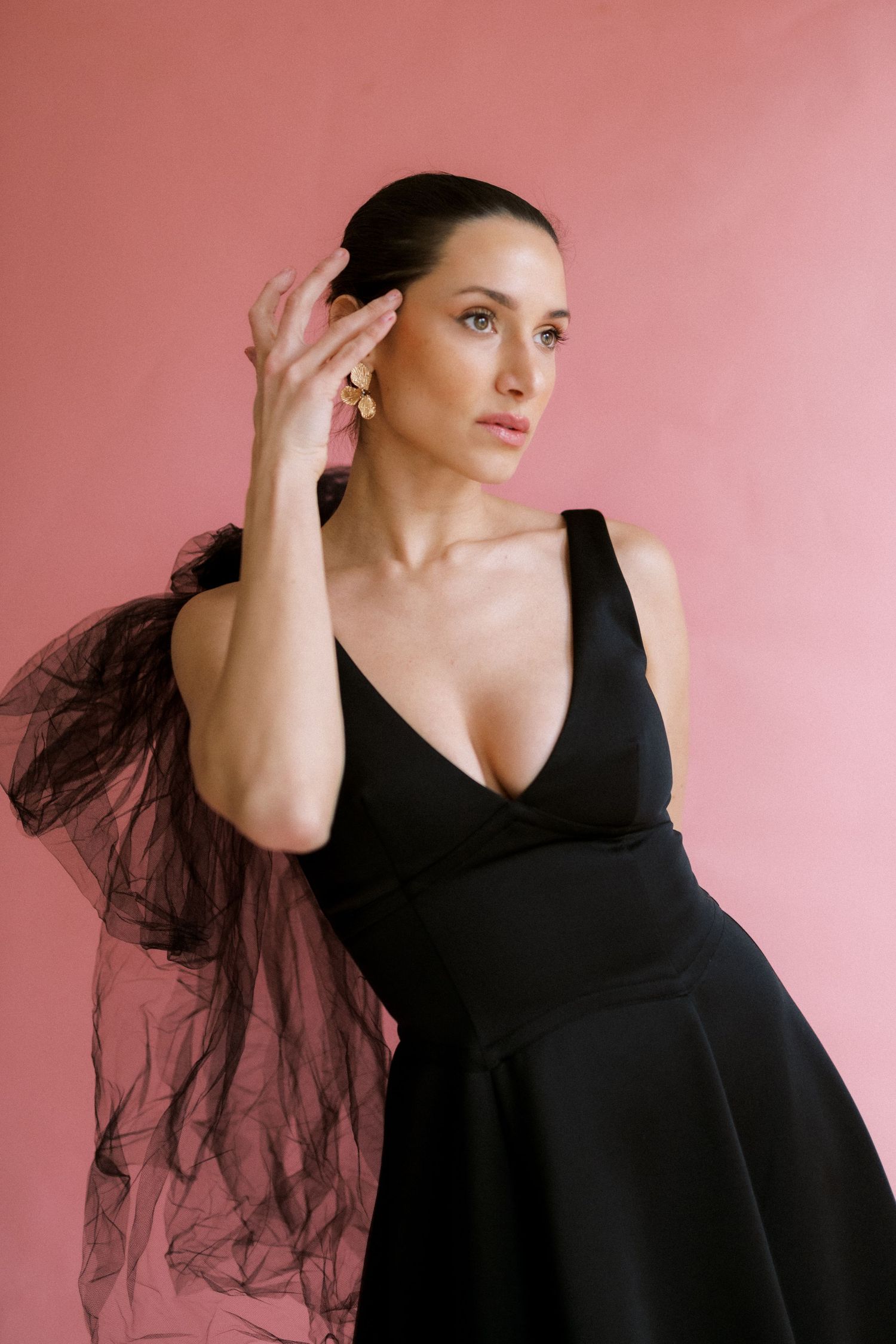 A portrait of someone in an elegant black dress with tulle details against a pink background.