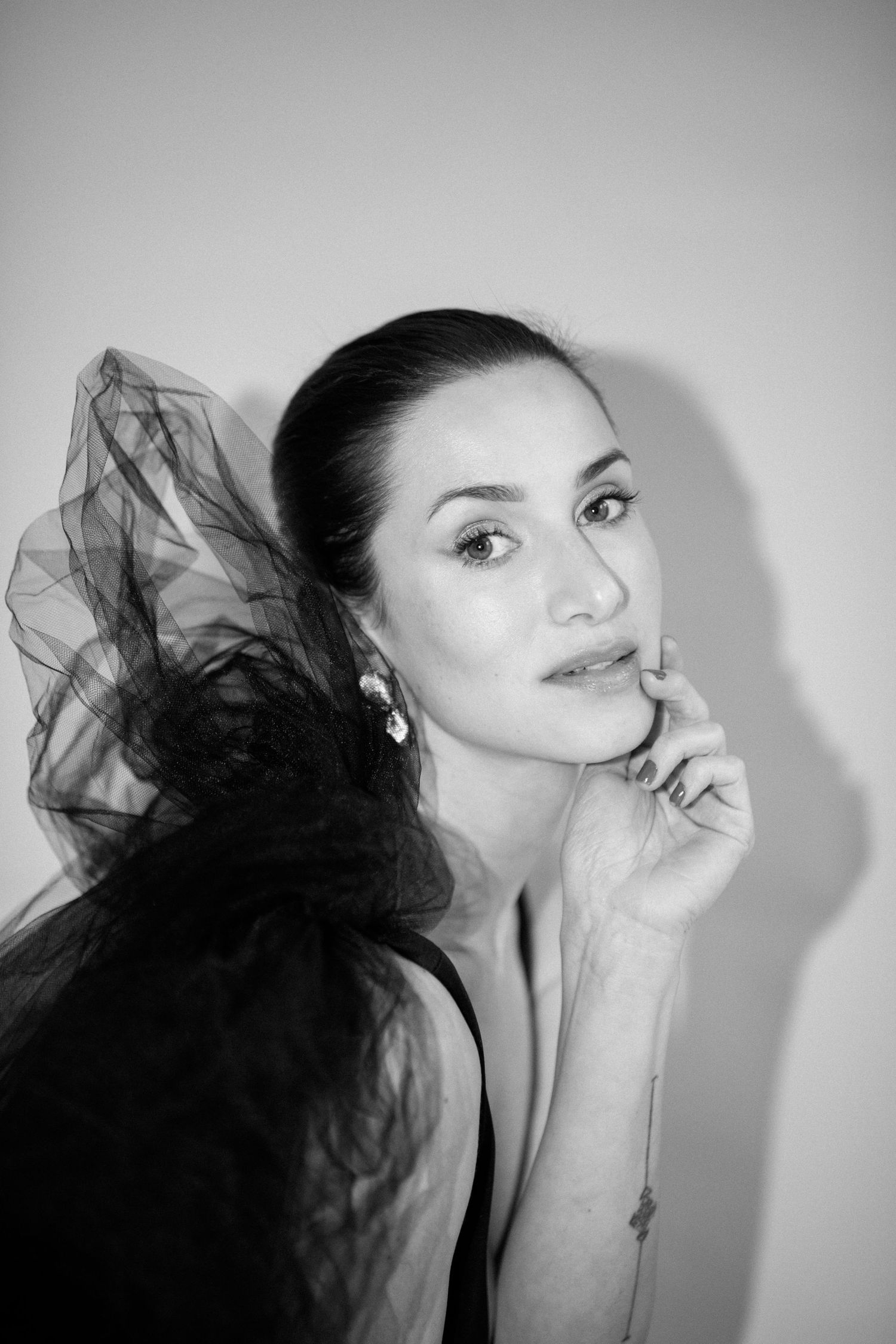 A black and white portrait showing a contemplative expression with elegant earrings and flowing sheer fabric.