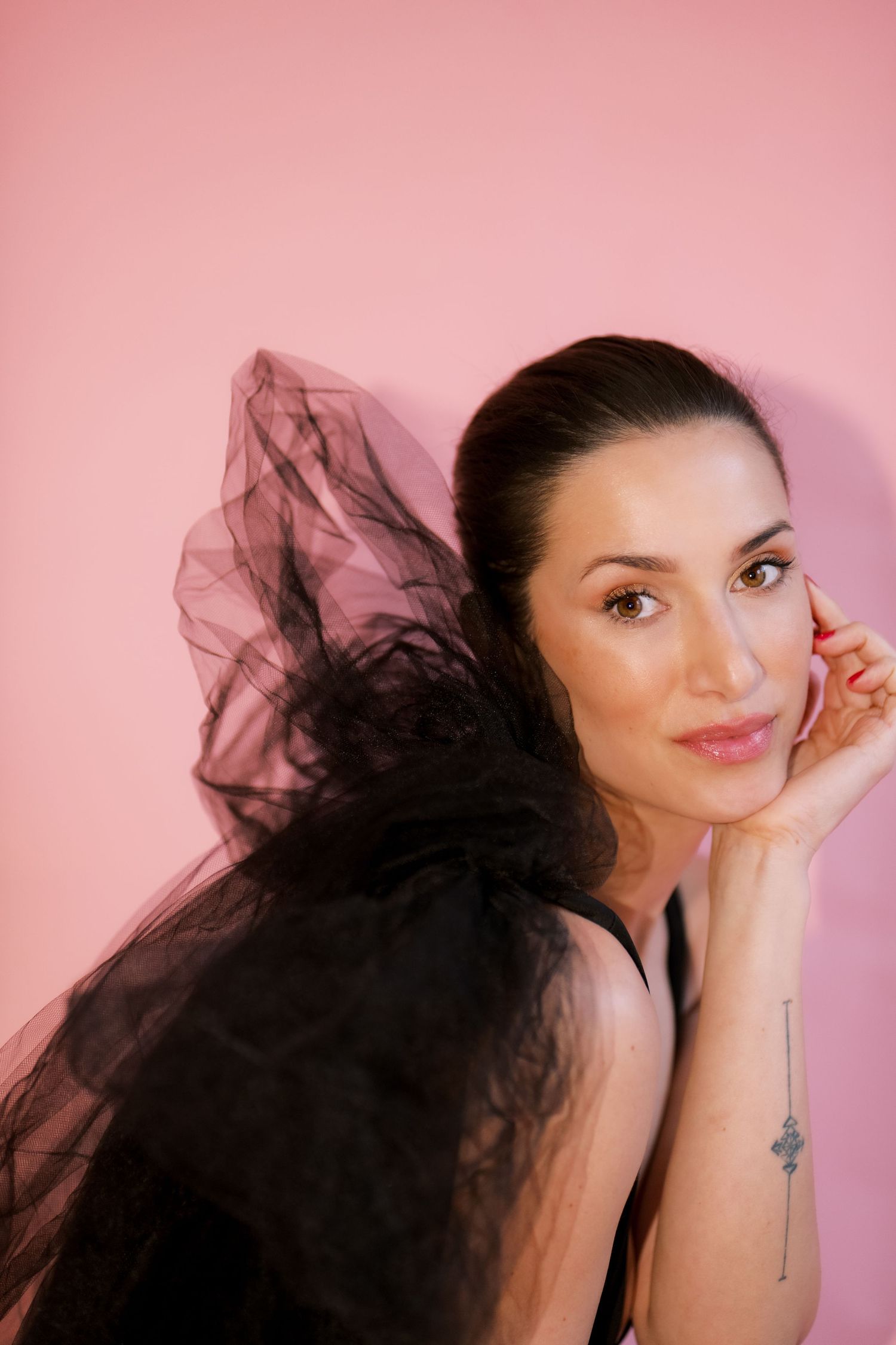 Portrait against pink background with flowing black tulle fabric and soft natural makeup.