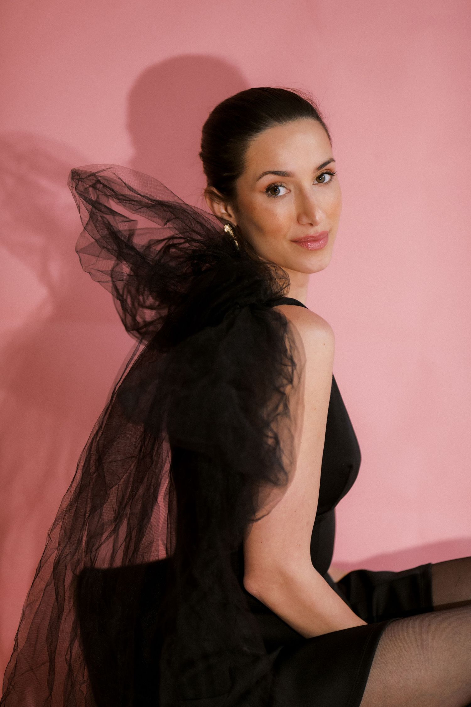 A woman in black poses elegantly with flowing black veil against a pink background, creating a dramatic portrait series.