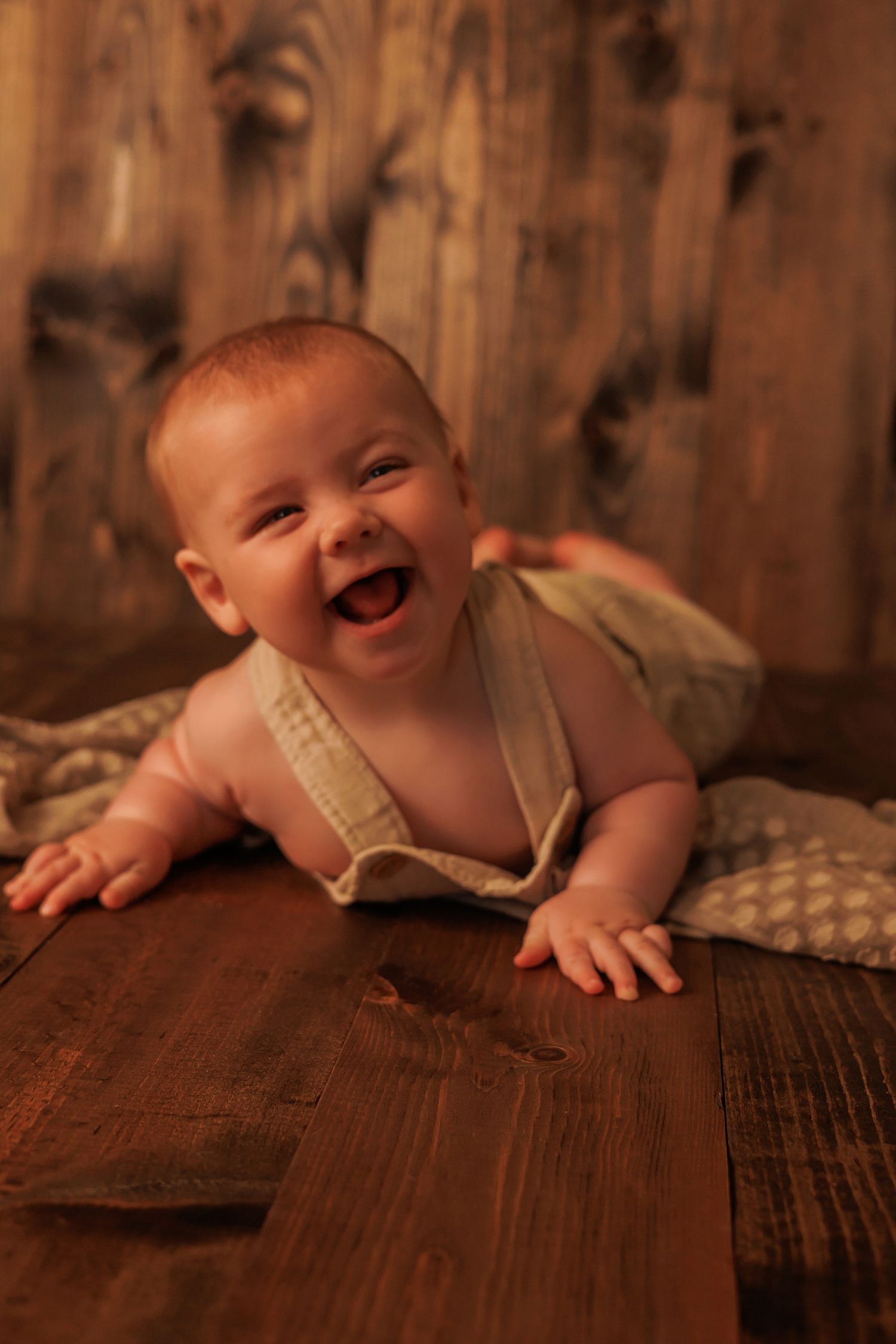 Series of artistic photos showing a baby lying on wooden floor with warm lighting and rustic background.