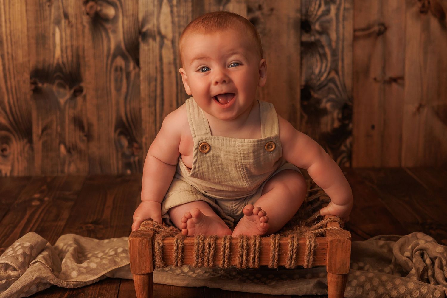 Milestone photography session with baby on wooden chair in rustic setting.