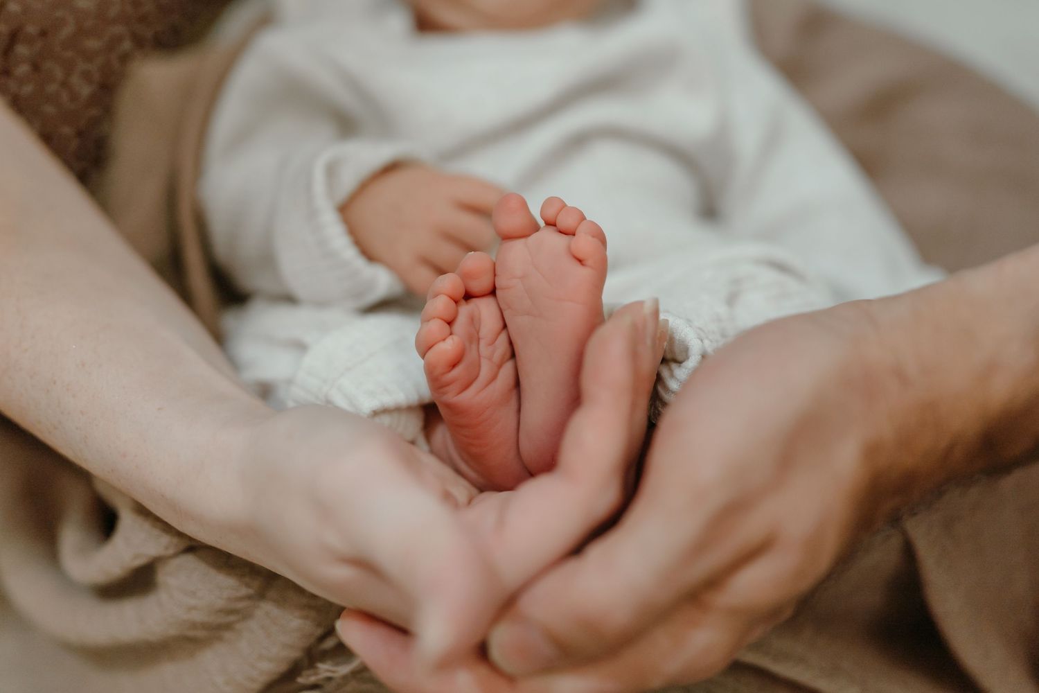 A close-up shot of tiny baby feet being gently held by adult hands against a soft brown blanket.