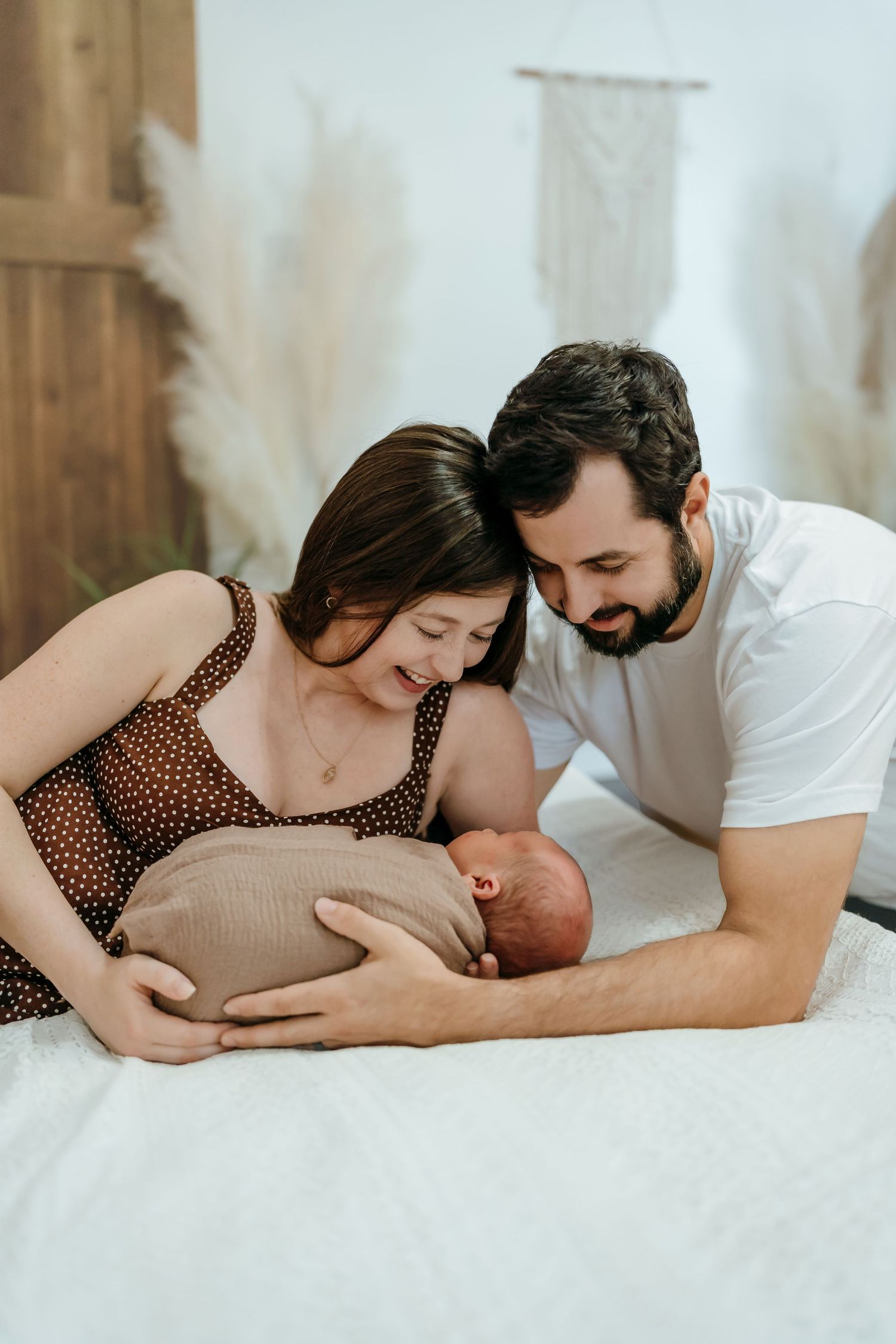 Tender moment captured in sequence showing couple embracing newborn baby while lying on white bedding.