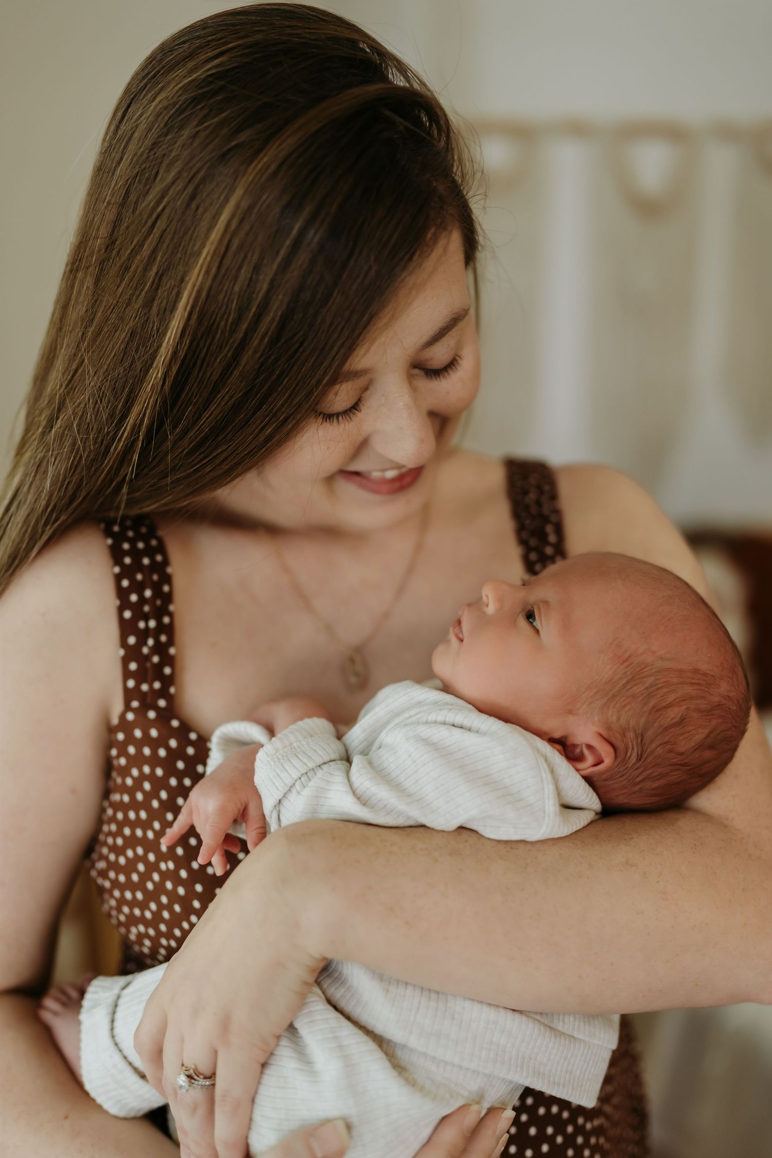 A tender moment of comfort and connection as a parent in a polka dot dress holds their sleeping newborn baby in white clothes.
