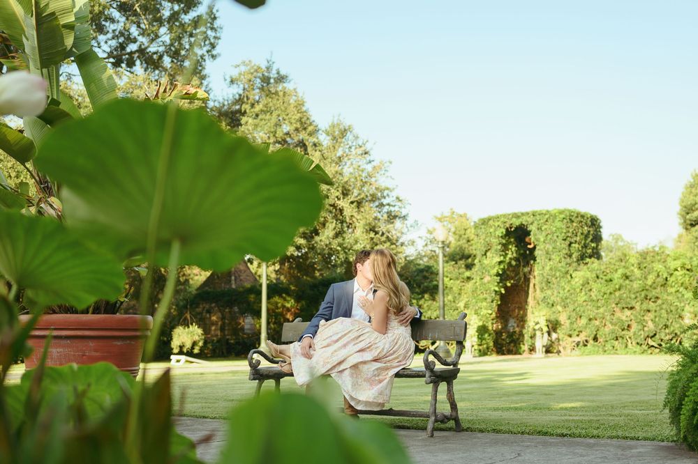 A dreamy garden scene where someone in a flowing dress relaxes on a bench surrounded by lush greenery and filtered sunlight.
