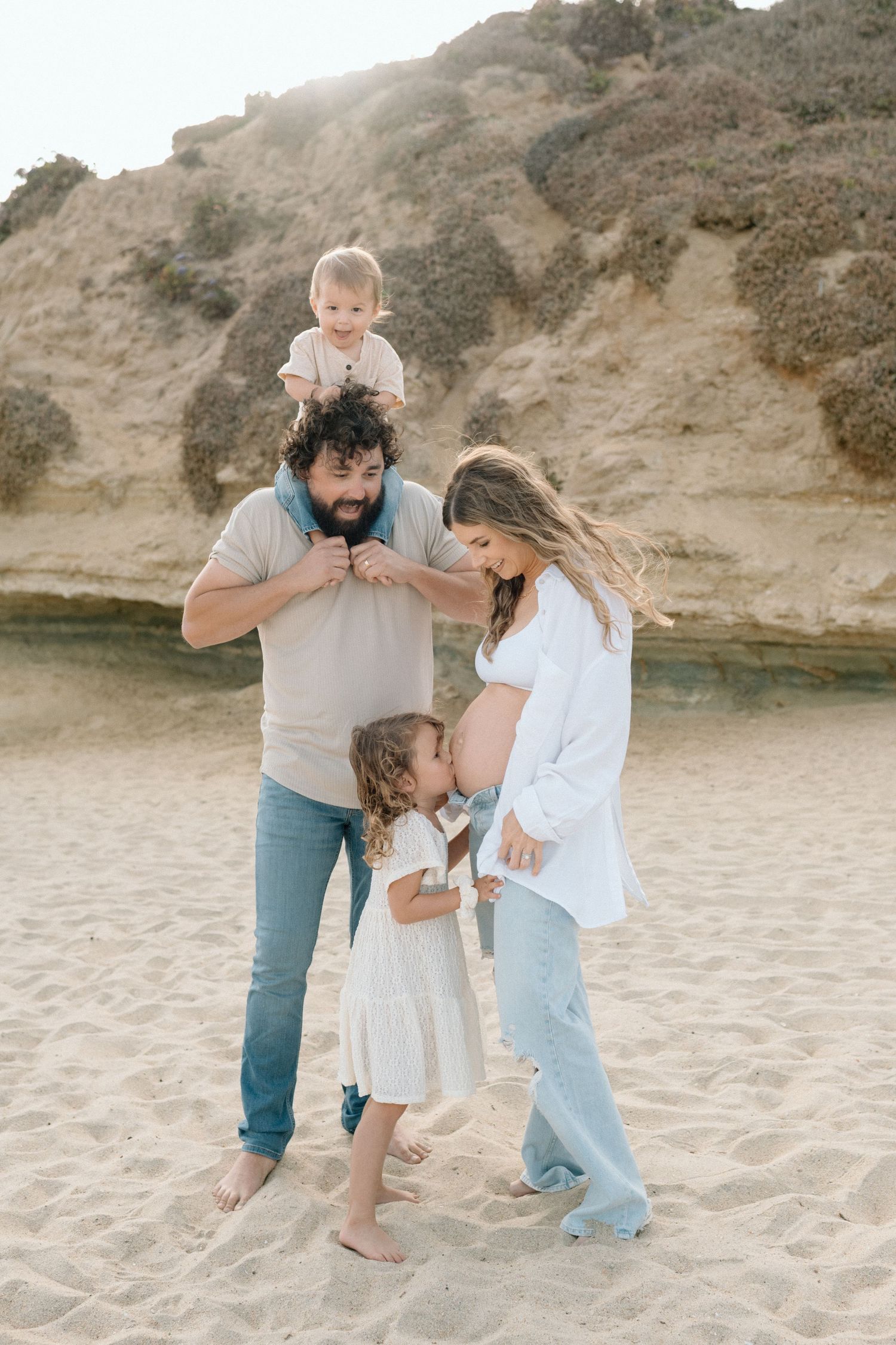 A loving family shares playful moments together on a sandy beach near rocky cliffs at sunset.