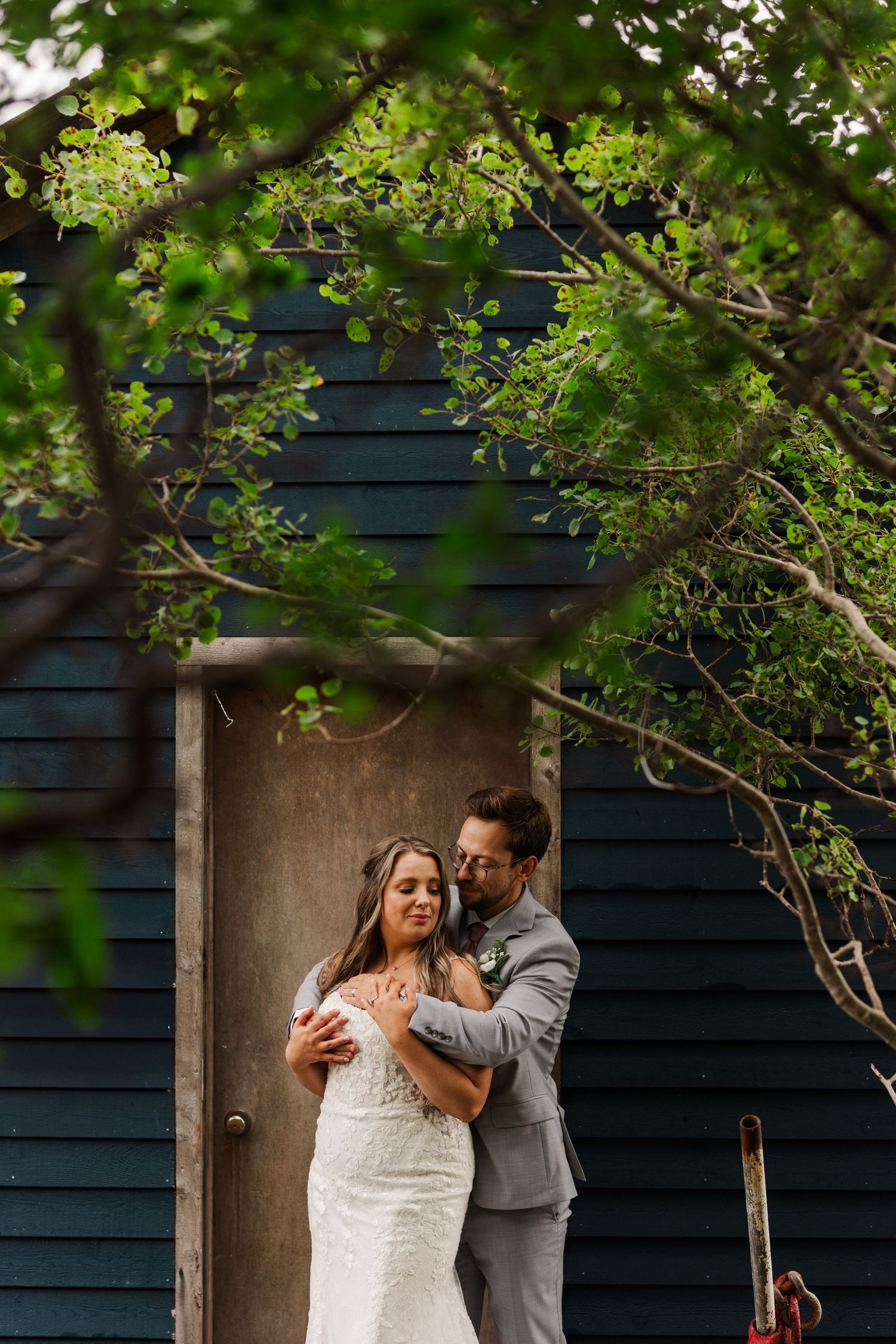 A romantic moment unfolds under green tree branches against a dark navy exterior wall.
