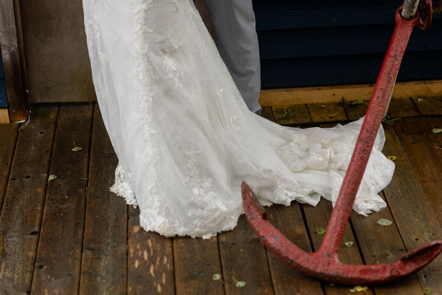 Side view of a delicate white wedding dress hanging from a rustic wooden wall or door frame.