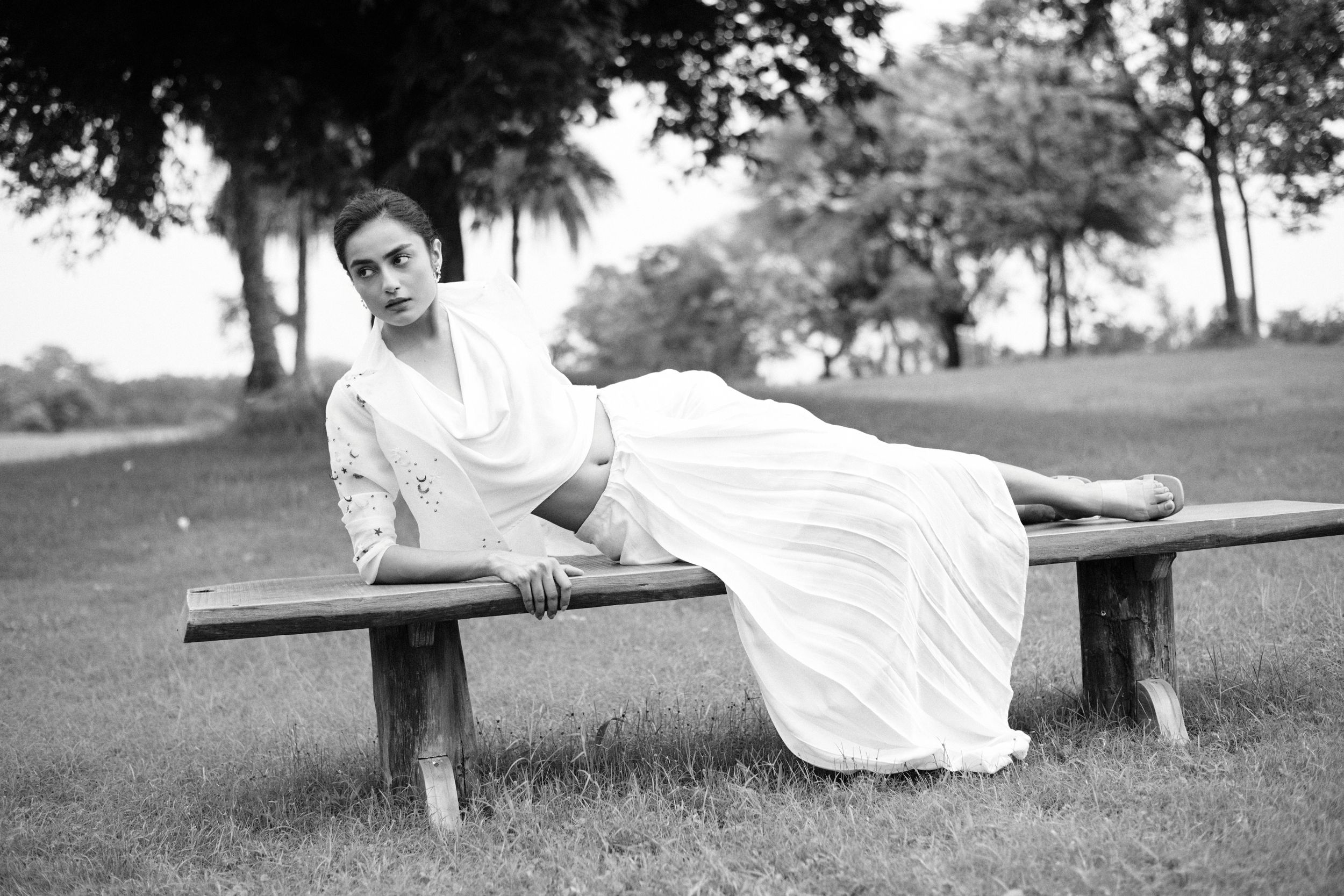 Full-body black and white shot of a model in a draped gown, poised against a plain backdrop.