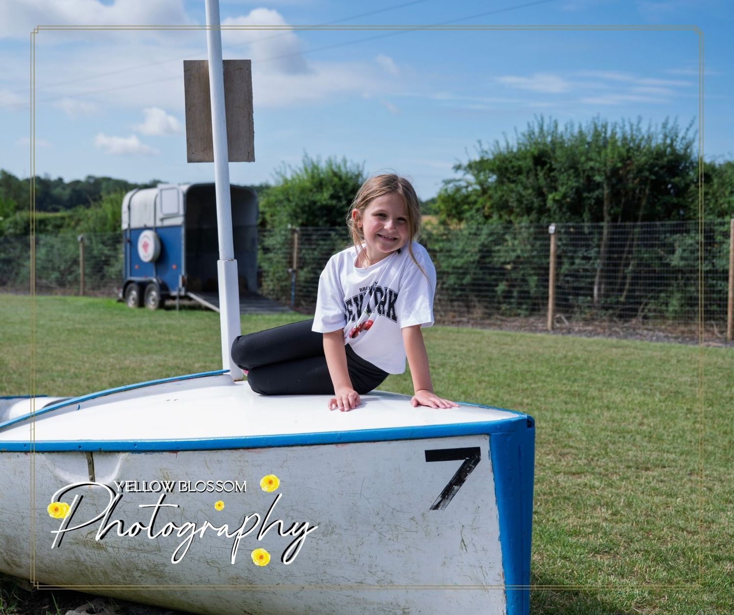 Young karate student in white uniform sits on ground next to white fence in outdoor training area.