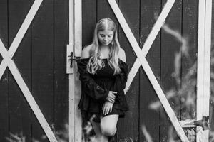 Black and white portrait of a person standing in front of a rustic barn door with white X-shaped beams.