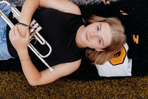Person lying in autumn grass while wearing black text t-shirt and holding cell phone.