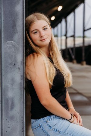 Portrait session in industrial setting with blonde hair and black top against concrete columns and natural lighting.
