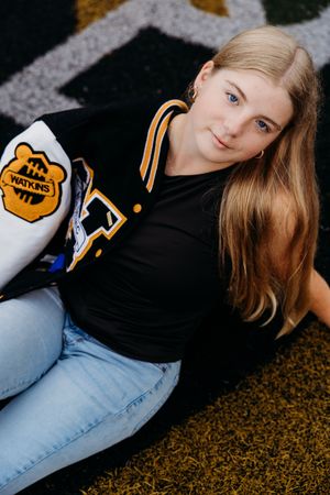 Person in black sweater with yellow accents and light jeans lounges on brown textured carpet for casual photoshoot series.