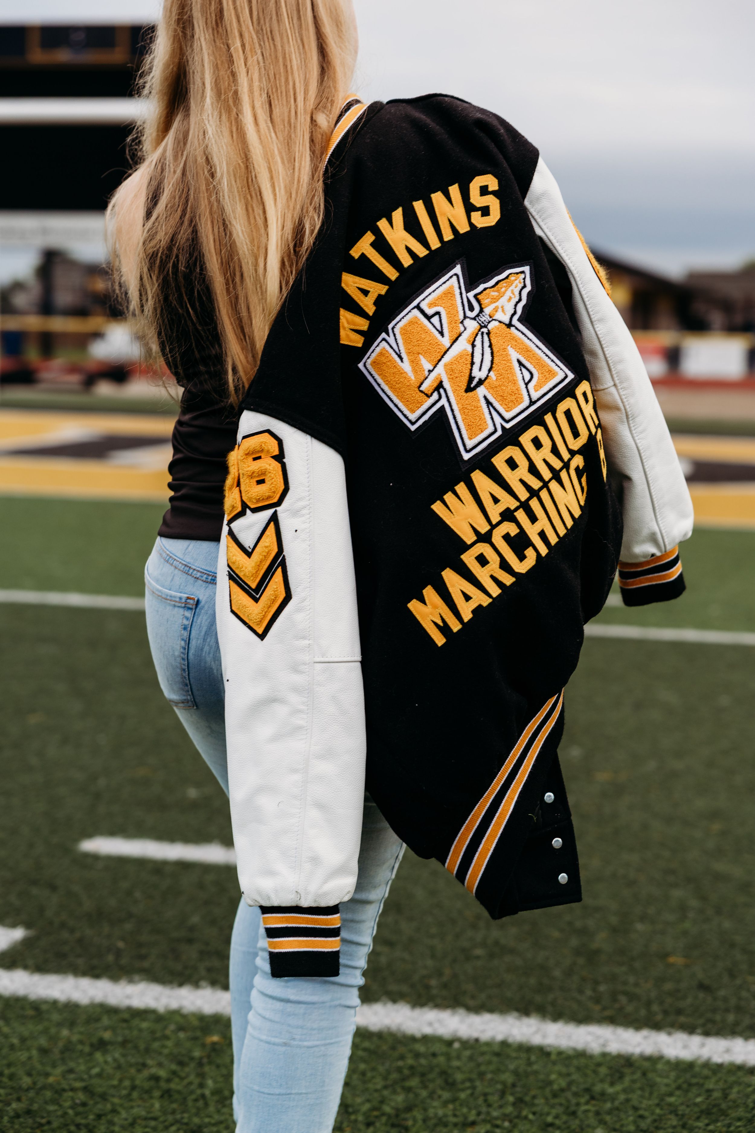 Black and white varsity letterman jacket with gold accents displayed in a series of close-up shots on a football field.
