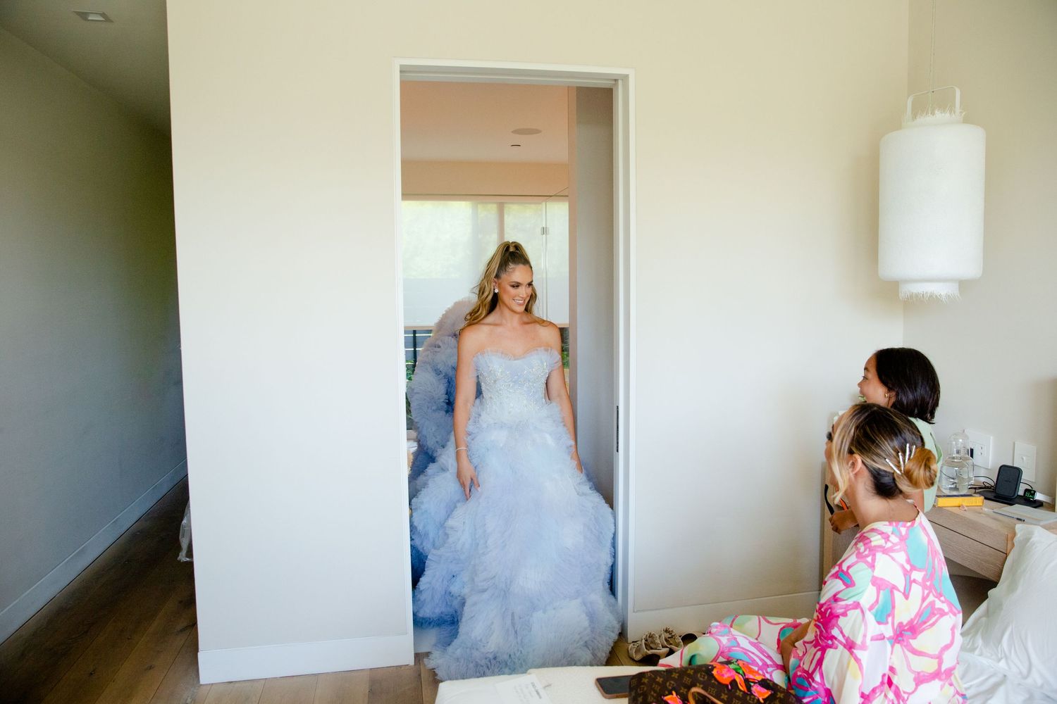 Person in blue tulle gown emerging from doorway during wedding preparation.