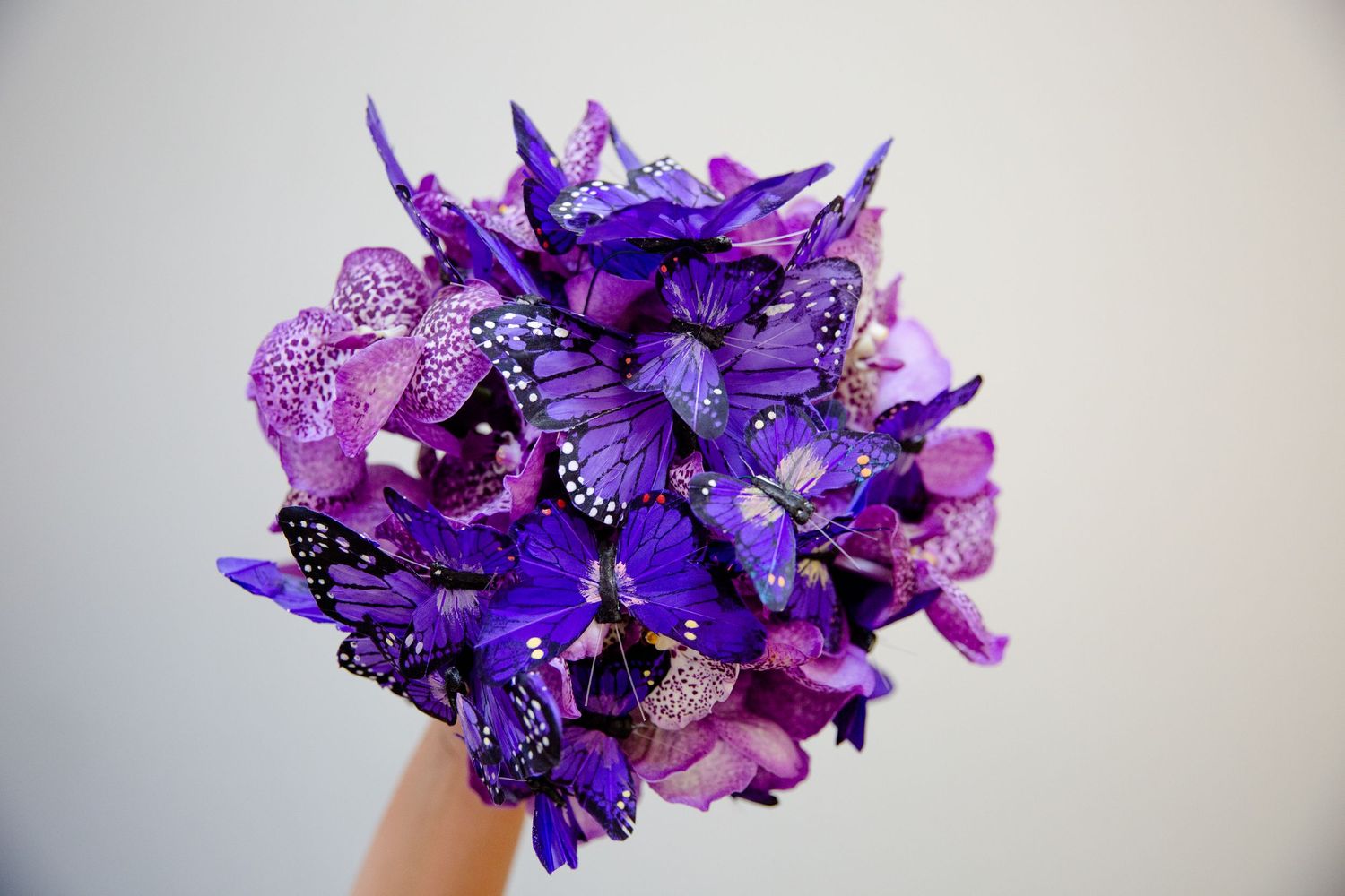 Stunning purple and lavender wedding bouquet with orchids and butterflies against gray background.