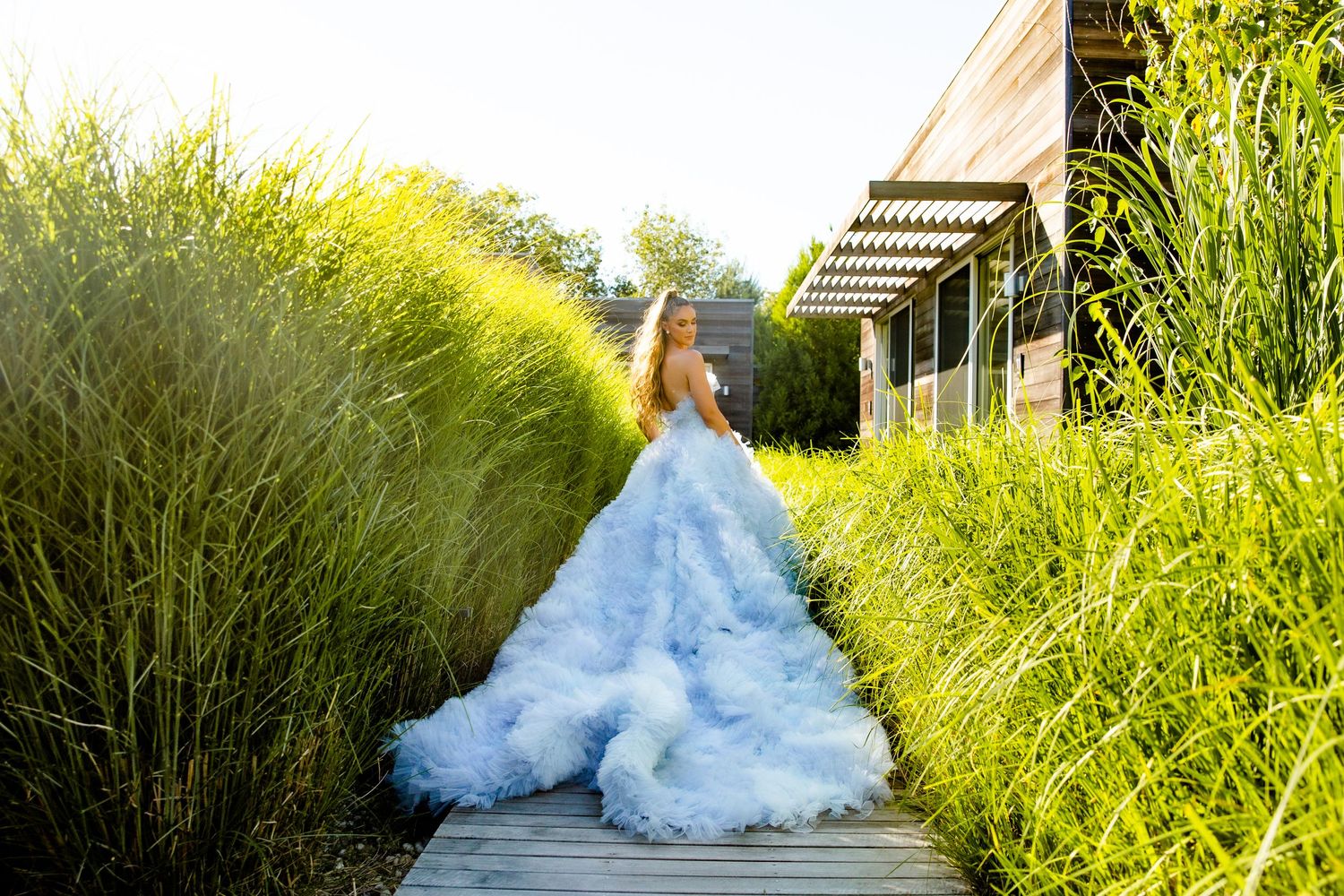 A dramatic blue and white wedding gown photographed against vibrant green landscaping.