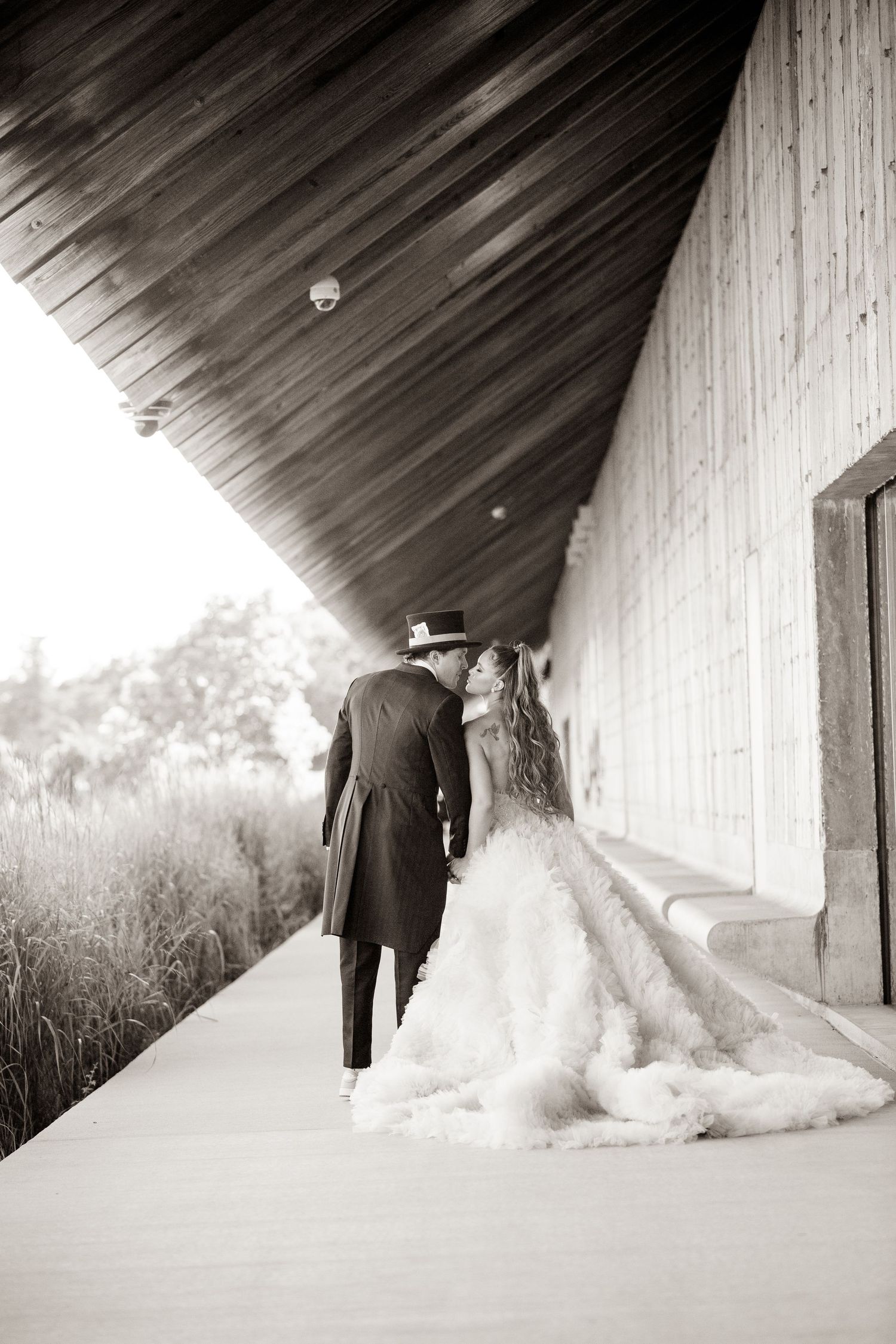 Artistic black and white photo of newlyweds walking along a covered pathway.