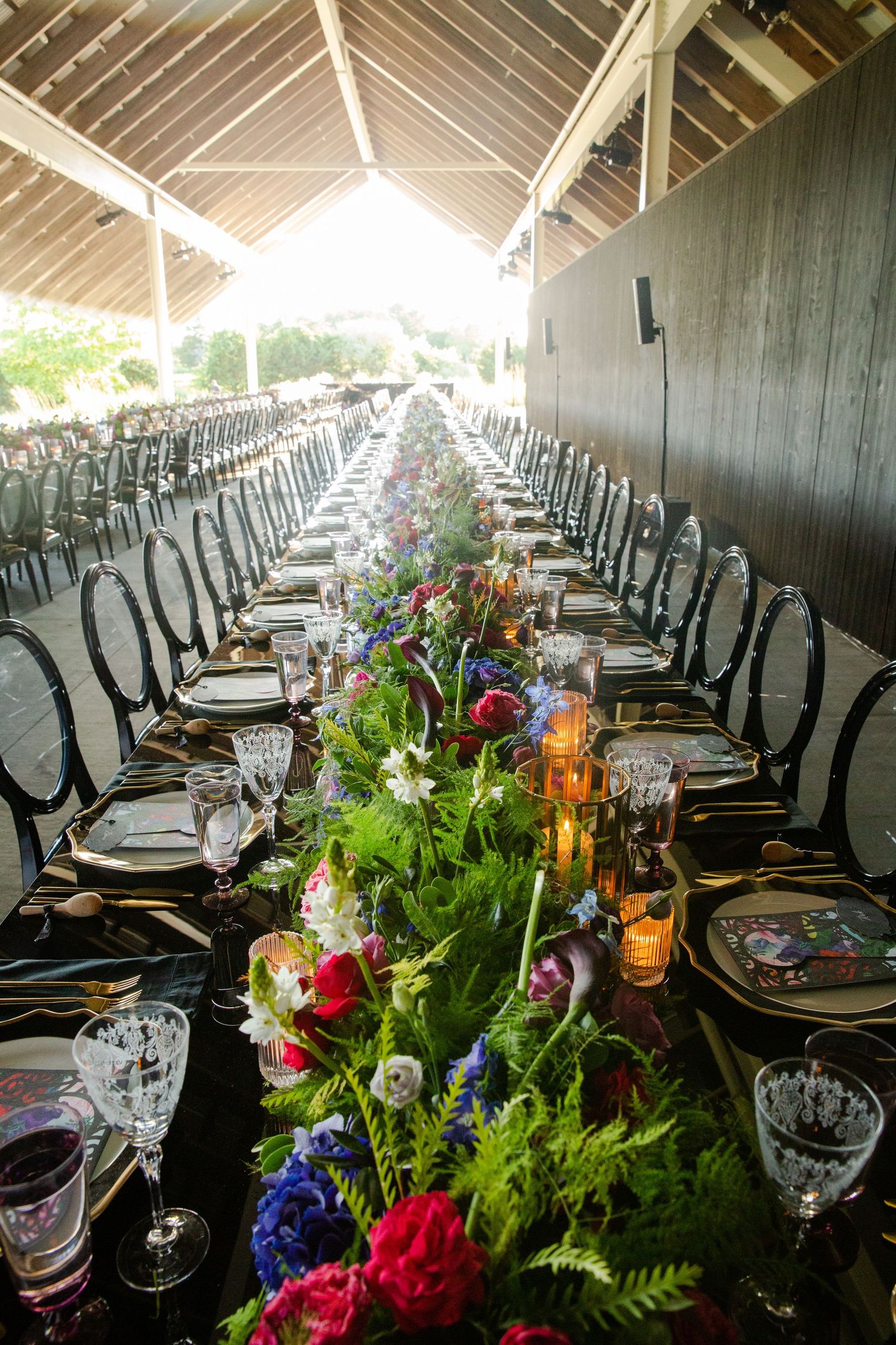 Elegant long dining table with vibrant floral runner and crystal glassware under wooden beams.